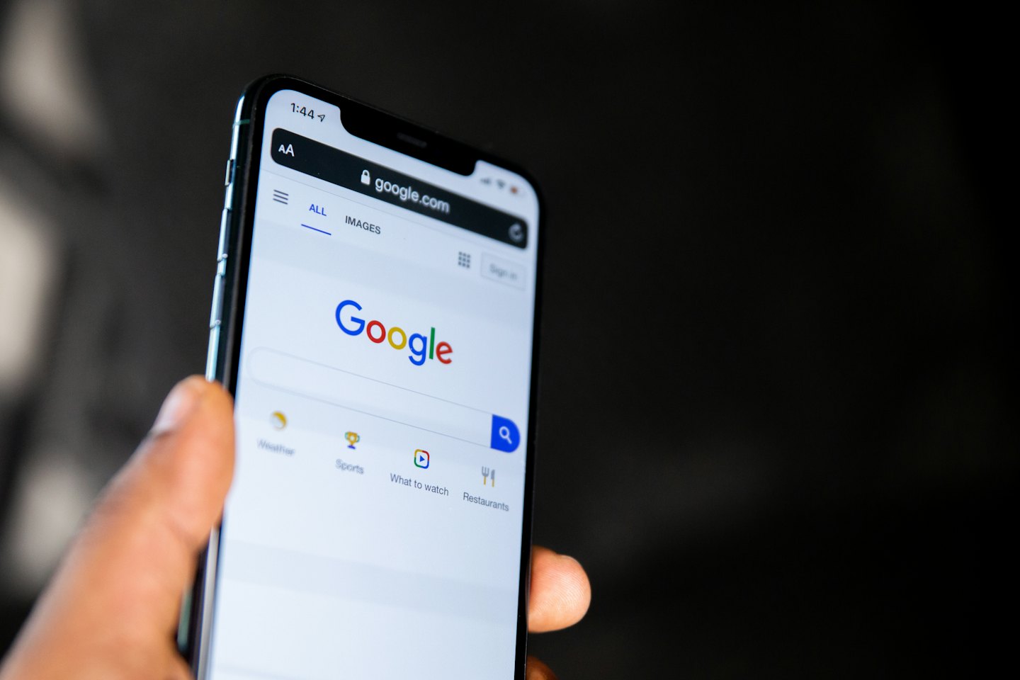 Hand holding a smartphone showing the Google search page.