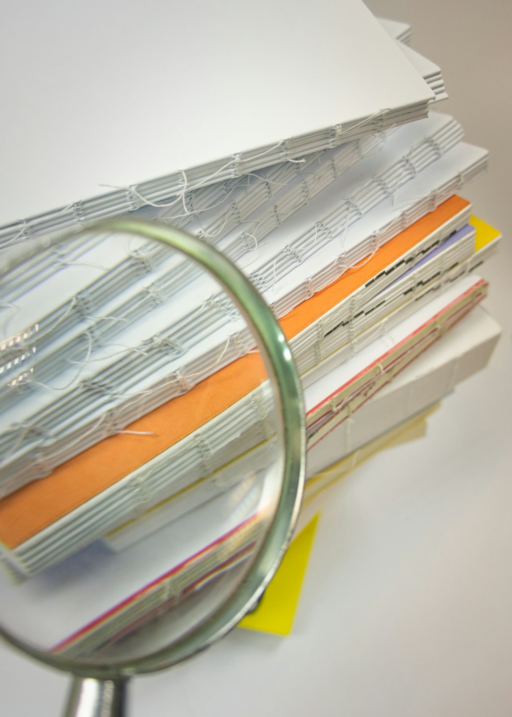 A magnifying glass rests on colorful bound document spines.